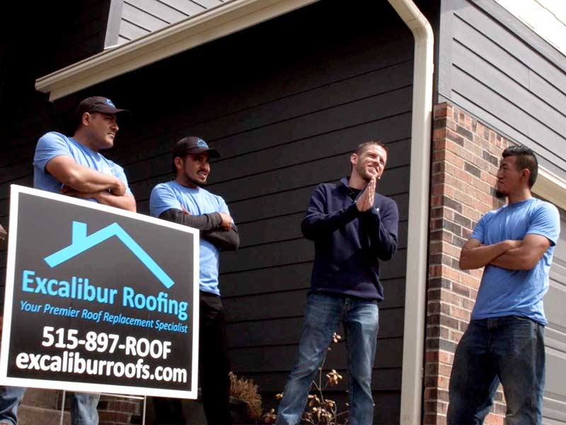 Excalibur Roofing team members in front of a home they just worked on and next to one of their front lawn signs with their logo, phone number, and website link
